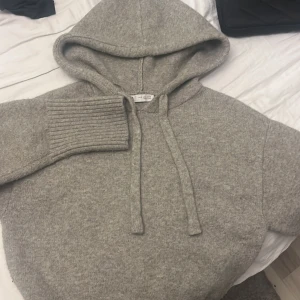 Grå hoodie från Zara - Säljer en stilren grå hoodie från Zara i storlek S.Den är tillverkad i ett mjukt material med ribbade muddar och en praktisk huva med dragsko. Perfekt för en avslappnad look. 
