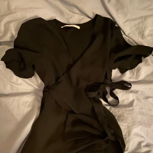 Svart omlottblus från Zara  - Snygg svart omlottblus från Zara  med korta ärmar och knytband i midjan. Perfekt för en stilren look.