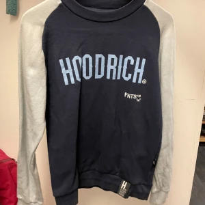 Blå dress från Hoodrich - Säljer en blå dress från Hoodrich med textdetaljer på både fram- och baksidan. Tröjan har en avslappnad passform och är perfekt för en casual look.