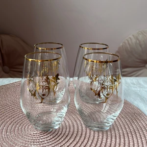 4 st Carolina Gynning guld glas  - Fyra stilrena glas med vackra gulddetaljer och ett konstnärligt ansiktsmotiv. Perfekta för att ge en lyxig känsla till dukningen. Glasen har en rundad form och en gyllene kant upptill. Från Carolina gynnings serie  ”Allglas Slice of Life Gold 35 cl”