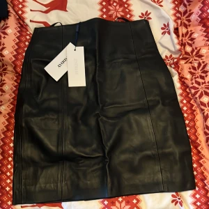 Svart skinnkjol från Andamane - Snygg svart skinnkjol från 2NDDAY i storlek 32. Kjolen har en stilren design med en rak passform och är tillverkad av naturligt djurskinn. Perfekt för en trendig look (PS! ordinarie pris 2000kr) . (OBS! Har inga bilder då jag köpte för liten storlek och får då inte på mig den)