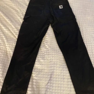 Svarta byxor från Carhartt - Snygga svarta byxor från Carhartt med raka ben, dem har en blek fläck på ena bakfickan och fyra små hål på insidan av midjan. Dem är köpta begagnade men aldrig använda av mig.