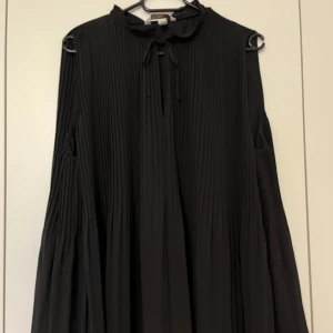Top, H&M, svart, L - Svart plisserad top från H&M i storlek L. Ny, oanvänd. Ingen prislapp kvar. 100% polyester. Längd ca 65 cm. A-formad.