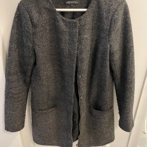 Grå kappa från ONLY - Snygg grå kappa från ONLY med rund hals och knäppning framtill. Den har en stilren design med två praktiska fickor.