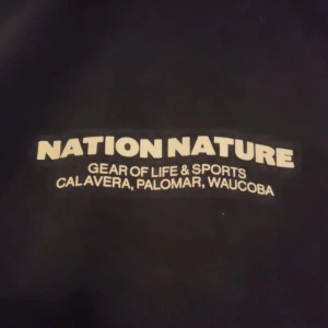 Svart hoodie från Nation Nature - Säljer en svart hoodie från Nation Nature med tryck på bröstet och ryggen. Tröjan har en klassisk känguruficka och justerbar huva med snören. Perfekt för en avslappnad stil.Den har lite fläckar men ingen märker .Pris kan diskuteras 