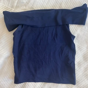 Mörkblå offshoulder topp från Kappahl - Säljer en stilren mörkblå offshoulder topp från Kappahl. Perfekt för en trendig look med sin åtsittande passform. Toppen är tillverkad i ett mjukt och bekvämt material.