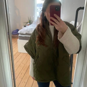 Grön quiltad cape/poncho - Säljer en grön quiltad capen med halfzip. Jackan har en oversized passform och är perfekt för kyligare dagar. Den har praktiska fickor och en stilren design. Använd endast en gång köpt för 1100kr