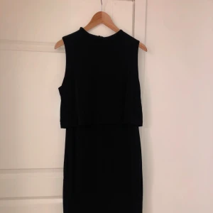 Svart ärmlös klänning med randig detalj - Elegant svart ärmlös klänning med vita och svarta ränder längst ner. Perfekt för en stilren look.