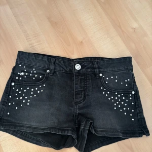 Svarta jeansshorts med pärlor - Snygga svarta jeansshorts dekorerade med pärlor på framsidan. Perfekta för en trendig look. 
