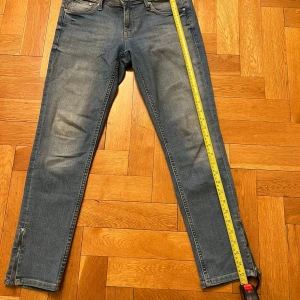 Blå jeans med slim ankle - Snygga blå jeans med slim ankle och låg midja. Perfekta för en avslappnad stil. Tillverkade i Pakistan med en klassisk femficksdesign och dragkedja. Passar bra till sneakers eller boots.