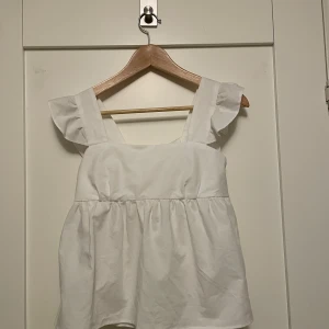 Vit topp med volangdetaljer - Säljer denna toppen med volangdetaljer på axelbanden och knytning i ryggen. Den är aldrig använd.💕