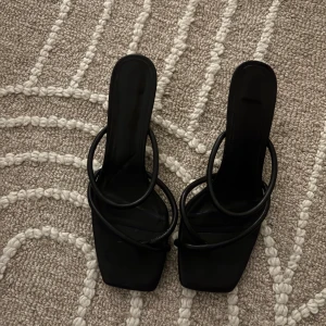 Svarta klackskor med remmar från nakd  - Eleganta svarta klackskor med smala remmar och fyrkantig tå. Perfekta för en stilren look.