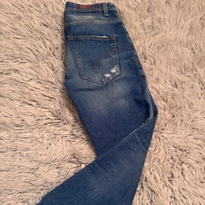 Slitna blå jeans från Dondup - Säljer dessa asfeta blå jeans med slitna detaljer från dondup. Det klasssiska Dondup stygnen på baksidan är röd vilket ger en snygg detalj. Storleken är w29. Bilderna blev lite konstiga men det är tagna själv. Hör av dig vid minsta fråga eller fundering😄.