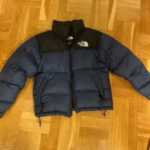 North face 1996 Retro Nuptse Jacket - Säljer en blå och svart pufferjacka från The North Face.