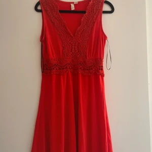 Röd klänning från Body Flirt - Snygg röd klänning från Body Flirt med v-ringad spetsdetalj framtill. Klänningen är ärmlös och har en elegant passform som passar perfekt för festliga tillfällen.