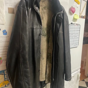 Svart skinnjacka från Trapper - Snygg svart skinnjacka från Trapper med mjukt foder och dragkedja. Perfekt för kyligare dagar med sin stilrena design och bekväma passform. Jackan har långa ärmar och detaljerade sömmar som ger en extra touch. Strl 52.