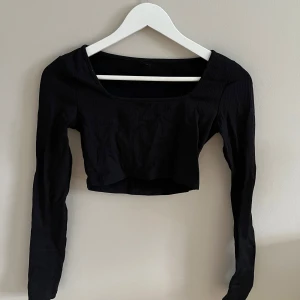 Svart ribbad croppad topp - Snygg svart ribbad topp med lång ärm och croppad design. Perfekt för en trendig look.