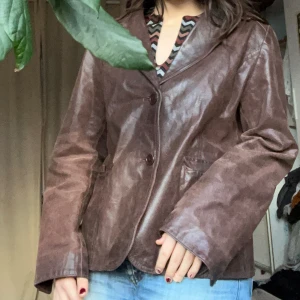 Brun skinnjacka med knappar - Snygg brun skinnjacka med knappar framtill och klassisk krage. Jackan har en normal passform och långa ärmar. Perfekt för höst och vår. Storlek L i mansstorlek men blir snyggt oversized på mig som är M i kvinnostorlek.