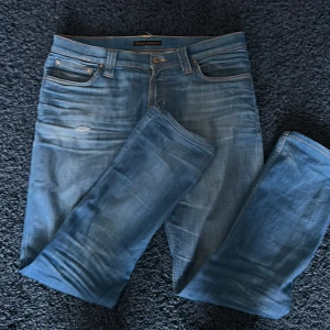 Nudie jeans - Snygga blå jeans från Nudie Jeans. Storleken matchar inte hur den egentligen passar och passar dig mellan 177cm och 183cm.  Har en slitning där fram (Bild.3) men de flesta brukar bara gilla det.                                                                          Hör av er vid frågor!                                                                                           Pris kan sänkas vid snabb affär👍🏻