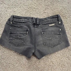 Grå jeansshorts från Pimkie - Snygga grå jeansshorts från Pimkie med fransiga kanter och klassisk femficksdesign. Perfekta för en avslappnad stil. Dekorativa sömmar på bakfickorna ger en extra touch. Midjemått: 37 cm