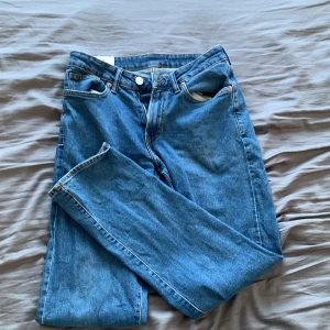 Blå jeans från H&M - Säljer ett par klassiska blå jeans från H&M i regular fit. De har en traditionell femficksdesign och är tillverkade i slitstarkt denim. Perfekta för en avslappnad stil. Det är slitage brevid båda bakfickorna men det syns bara vid uttöjning av området.
