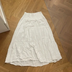 Vit långkjol från 157 - Säljer en vit långkjol från 157 med elastisk midja. Kjolen har en luftig och bekväm passform, perfekt för varma dagar. Den är tillverkad i ett lätt material som ger en skön känsla.