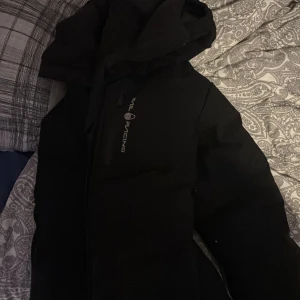 Svart dunjacka från Völkl Racing - Säljer en svart dunjacka från Sail Racing. Jackan har en stilren design med dragkedja och en hög krage för extra värme. Perfekt för kyliga dagar.äkta är den med 