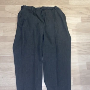 Grå kostymbyxor från M&S - Snygga grå kostymbyxor från M&S med en klassisk passform. Byxorna har en midwaist design och är perfekta för en stilren look. De har en enkel stängning med dragkedja och knappar.