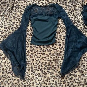 Svart topp med spetsdetaljer - Snygg svart topp med långa spetsärmar och en liten rosett framtill. Toppen har en tight passform och är perfekt för en elegant look. Den har en vacker spetsdesign som ger en extra touch av stil.