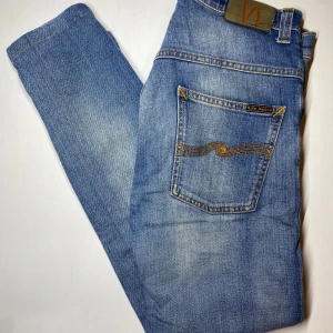 Nudie Jeans – Klassiska Blå Denimjeans  - Säljer nu dess eftertraktade nudie Jeans. De har en ljusblå tvätt med subtila slitningar Tillverkade av 100% ekologisk bomull.  Detaljer: 	•	Märke: Nudie Jeans Co 	•	Storlek: W31 	•	Längd: 95 cm 	•	Midja: 39 cm 	•	Färg: Ljusblå tvätt med diskreta slitningar 	•	Passform: Slim fit med klassiskt femficksdesign 	•	Material: 100% ekologisk bomull 	•	Tillverkade i: Italien 	•	Skick: Bra begagnat skick – inga hål eller fläckar  Pris: 349 kr (fast pris) Nypris: 1600kr