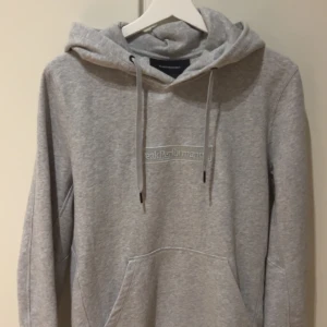 Grå hoodie från Peak Performance - Säljer en stilren grå hoodie från Peak Performance. Den har en klassisk design med en känguruficka och justerbar huva med dragsko. Perfekt för en avslappnad look.