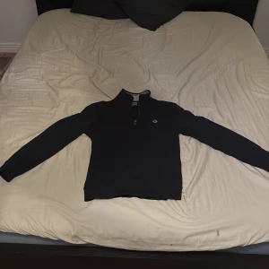 Svart tröja med halv dragkedja från Morris - Säljer en stilren svart tröja från Morris med halv dragkedja. Perfekt för en avslappnad men ändå snygg look. Tröjan har långa ärmar och en liten logga på bröstet. Passar bra till både jeans och chinos.