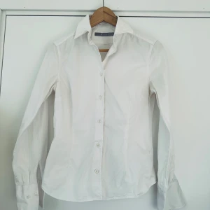 Vit skjorta från Tiger of Sweden - Säljer en stilren vit skjorta från Tiger of Sweden i storlek 38. Skjortan har långa ärmar och knappar framtill samt vid ärmsluten. Perfekt för en klassisk look. 🕊️