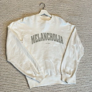 Vit sweatshirt  - Säljer en stilren vit sweatshirt från Vailent med texten 'Melancholia' i grått på framsidan. Tröjan har långa ärmar och en klassisk rund halsringning. Perfekt för en avslappnad look. Ljuset tröjan är tagen i får den se lite grå ut men den är helt vit.  Tröjans storlek är XS (Men den är oversize) så skulle säga att den är mellan S-M i storlek. Själv har jag storlek M o den passar bra inte för tajt.