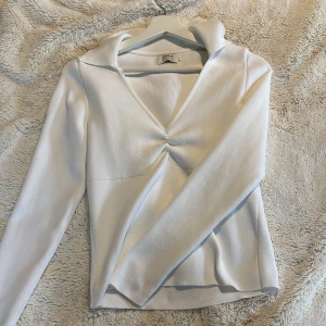 Vit ribbad tröja med krage - Säljer en stilren vit ribbad tröja från ONLY. Tröjan har en v-ringad design med en snygg rynkdetalj framtill och långa ärmar med krage. Jätte fint för en mer elegant stil