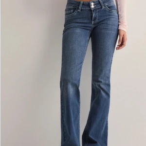 Blå bootcut jeans från Nelly - Snygga blå low waist bootcut jeans från Nelly med dubbla knappar i midjan och broderade detaljer på bakfickorna. Det är lite nedtrappade längst ner, annars inga defekter. 