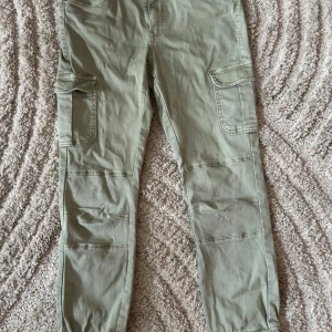 Gröna cargobyxor från ONLY - Snygga gröna cargobyxor från ONLY med praktiska fickor på sidorna. Byxorna har en avslappnad passform och är perfekta för en casual look. De har en knapp och dragkedja framtill.