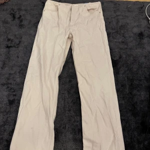 Beige byxor från Pull&Bear - Säljer ett par stilrena beige byxor från Pull&Bear. De har en klassisk design med dragkedja och knapp framtill. Perfekta för en avslappnad men ändå snygg look.