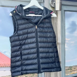 Svart väst från Tommy Hilfiger - Säljer min riktigt snygga Tommy Hilfiger väst i väldigt fint skick perfekt nu när våren börjar komma, avtagbar luva. 🤩 Storlek XS kan passa S,                                                                               Köpt från NK i Göteborg ordinarie pris: 2499kr mitt pris: 799kr   Vid snabb affär kan priset diskuteras  MVH Oliver