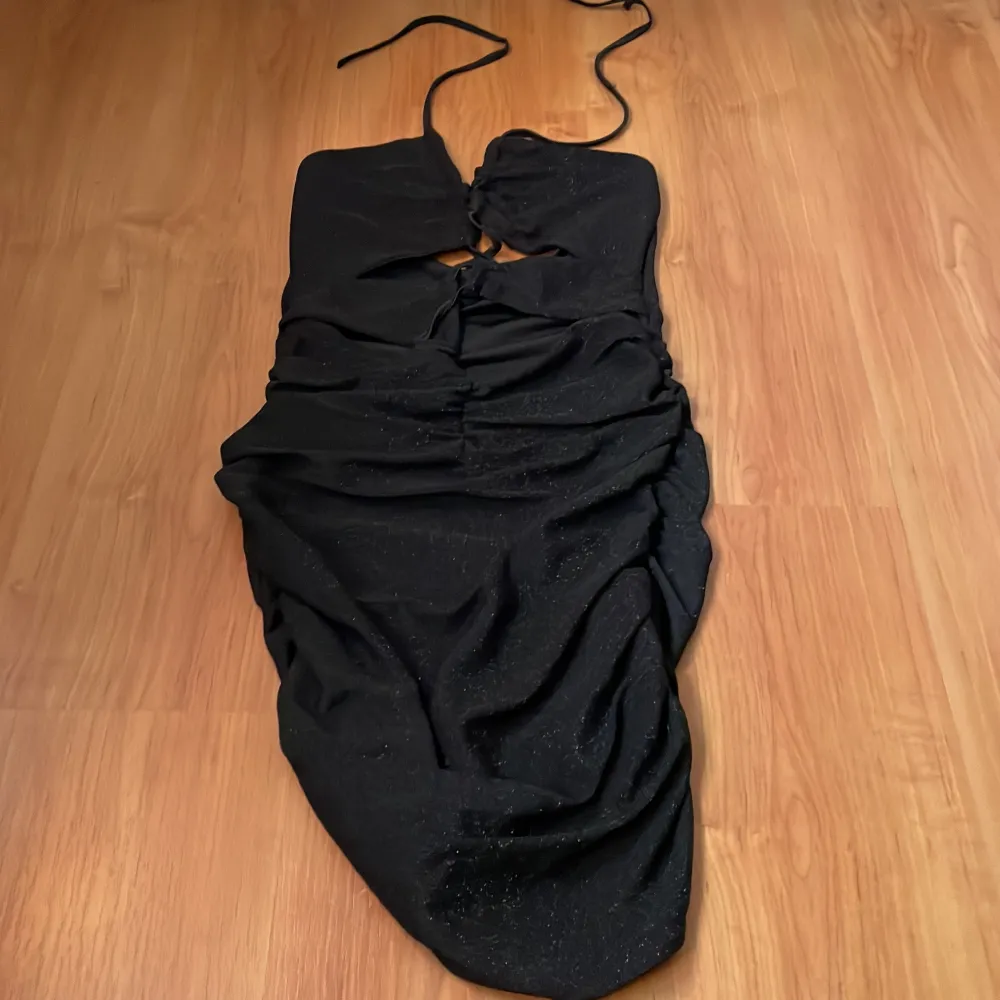 Snygg svart klänning med glittrande detaljer och smala axelband. Klänningen har en åtsittande passform och en elegant snörning framtill. Perfekt för en kväll ute eller en speciell tillställning.Testat den men aldrig haft på mig den någonstans.Den var för liten för mig.. Mekot.