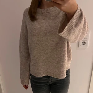 stickad tröja - Säljer en mysig beige/rosa stickad tröja med långa ärmar. Perfekt för kyligare dagar. Tröjan har en enkel design med ribbade muddar vid ärmslut och nederkant. Litet hål vid ärmen, syns nästan inte..