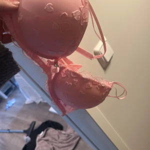 Rosa bh med hjärtmönster - Söt rosa bh med broderade hjärtan och justerbara axelband. Den har en mjuk vaddering för extra komfort och stöd. Perfekt för att lägga till en romantisk touch till din garderob. HELT NY BARA BORT TAGNA LAPPAR