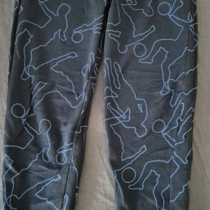 Grå byxor med blått mönster - Snygga grå byxor med ett unikt blått mönster av silhuetter. Perfekta för en avslappnad stil med en twist. Byxorna har en normal passform och är gjorda i ett bekvämt material.