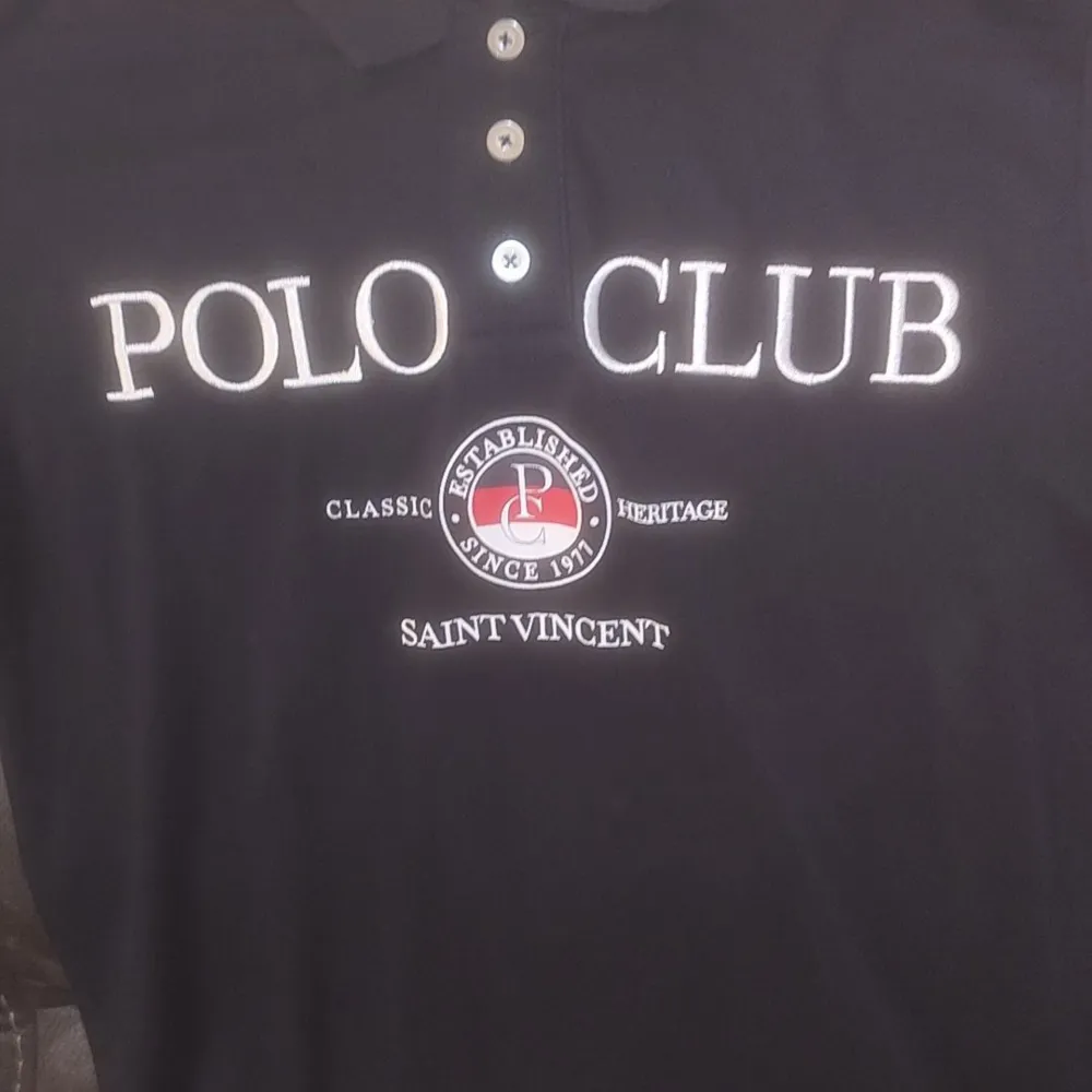Säljer en stilren svart pikétröja från Polo Club med broderad text på framsidan. Tröjan har en klassisk krage och knappar framtill. Perfekt för en avslappnad men ändå snygg look.. T-paidat.