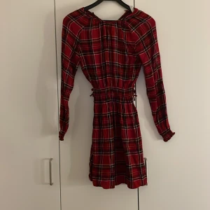 Rutig röd klänning - Säljer en snygg röd rutig klänning med långa ärmar och elastisk midja. Perfekt för höst och vinter med sitt klassiska rutmönster. Klänningen har en bekväm passform och är lätt att styla med olika accessoarer. OBS STOR GALJE! Storleken är 158 men passar xxs 