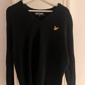 Svart tröja från Lyle & Scott - Snygg svart tröja från Lyle & Scott med v-ringning och deras  logotyp broderad på bröstet. Perfekt för en stilren look.