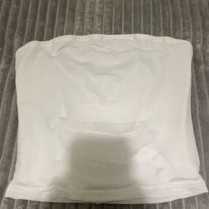 Vit tubtopp - Säljer en stilren vit tubtopp i ett tunt och stretchigt material. Perfekt för varma dagar eller som ett lager under andra plagg. Enkel och mångsidig design.