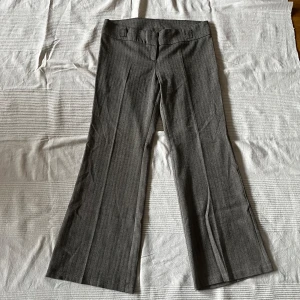 Grå kostymbyxor - Snygga grå kostymbyxor med diskret randigt mönster. Byxorna har en klassisk bootcut-stil och är perfekta för en stilren look. De har hällor för bälte och en elegant passform. Midjemåttet tvärsöver är 45 cm och innerbensmåttet är 79 cm🌟🌟
