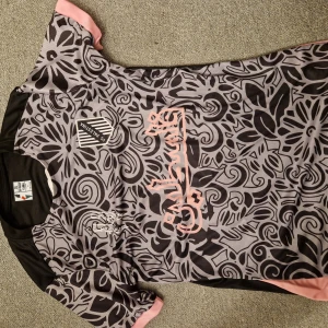 Mönstrad fotbollströja med rosa detaljer - Snygg fotbollströja med unikt svart mönster på grå bakgrund och rosa detaljer. Kortärmad design med rund hals och klubbmärke på bröstet. Perfekt för både träning och match!