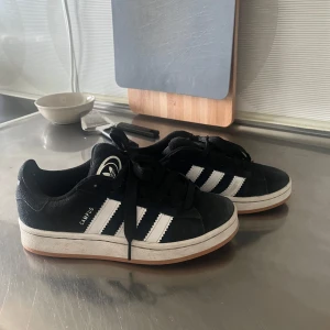Svarta Adidas Campus sneakers - Kan rengöra innan jag skickar iväg dem, använda max 10 gånger, nypris 1300 kr. Snygga Adidas Campus sneakers. Skorna har en vit sula och svart snörning. Perfekta för en avslappnad stil.